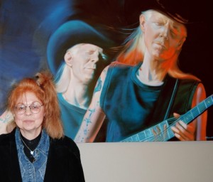 Samantha Wendell with her portrait of Johnny Winter (one of many rock artists she has painted) at the colony’s first art exhibit, “Reimagining Life.”