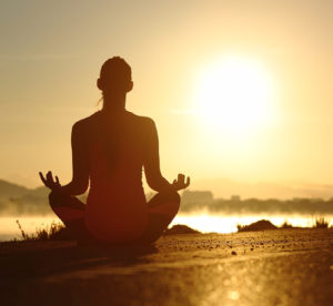 Silhouette of a fitness woman exercising yoga meditation exercises with the sun in the background